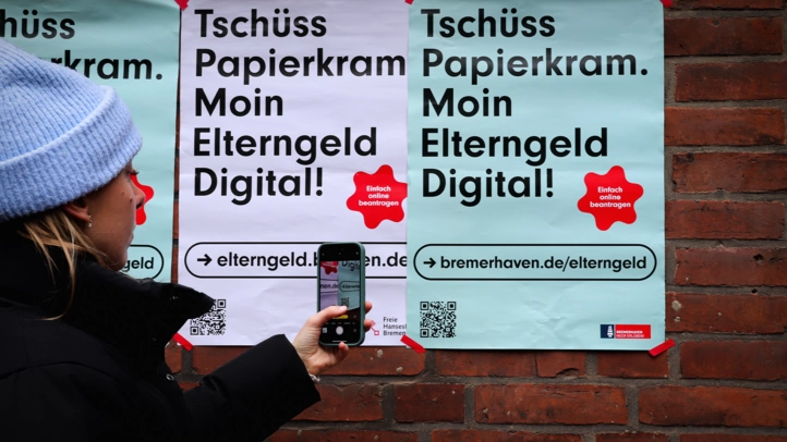 Eine junge Frau fotografiert den QR-Code der ElterngeldDigital Kampagne Bremen von einem Straßenplakat.