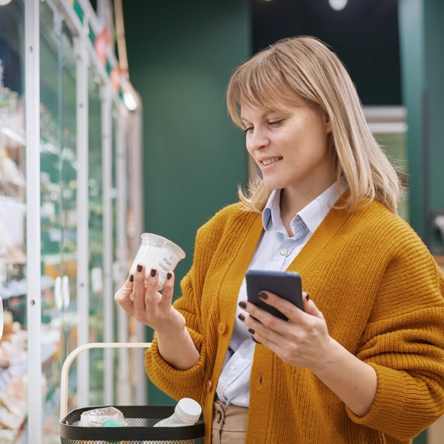 Eine Frau im Supermarkt auf ihr Smartphone blickend.