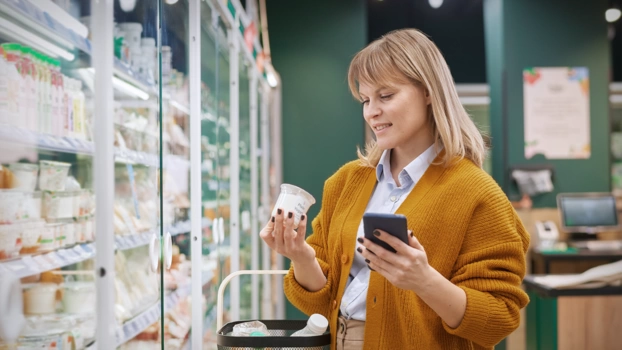 Eine Frau im Supermarkt auf ihr Smartphone blickend.