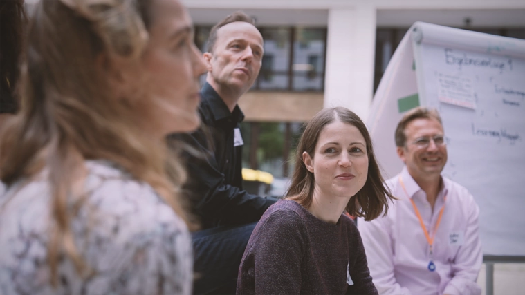 Vier Mitarbeitende in einem Workshop. Sie hören aufmerksam einer referierenden Person zu.